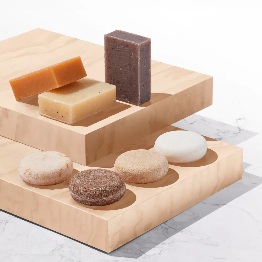 An arrangement of rectangular soap bars and round shampoo bars on wooden platforms with a marble background.